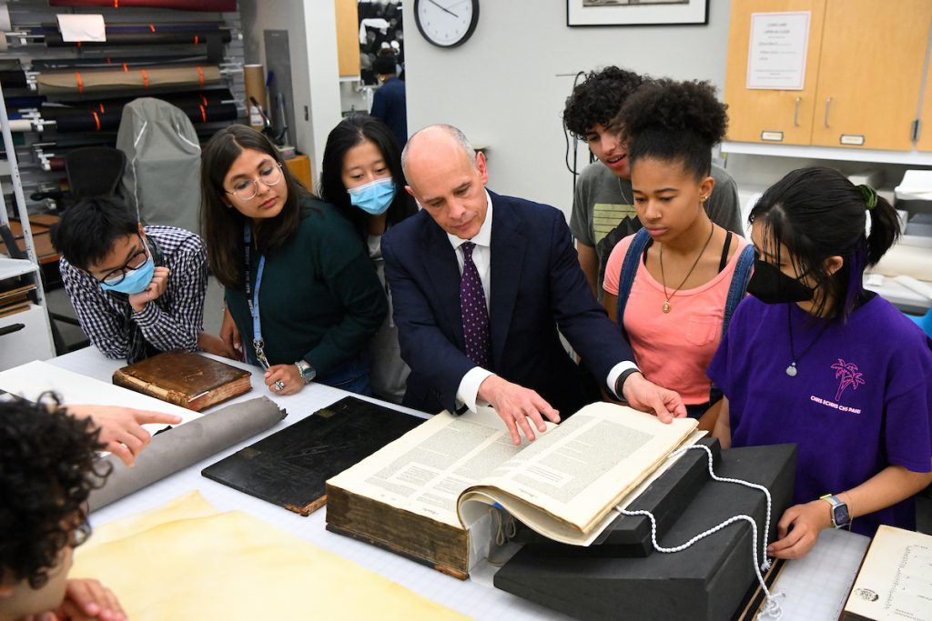 Students gathered around their professor examining a rare book in the library.