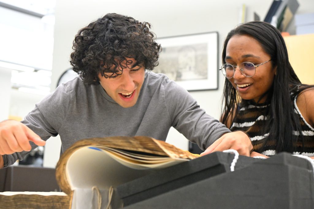 Two students smiling, leaning over a large book.